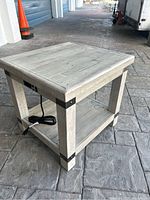 Side angle view of the light-colored wooden end table showing the integrated power outlet and power cord.
