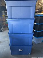 Stack of four large blue plastic rolling storage totes with lids, visible wear and minor scuff marks.