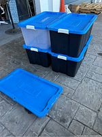 Stacked three storage bins, two black opaque and one translucent, all with blue lids. One blue lid off to side.