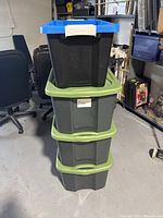 Stack of four medium plastic totes: three gray with green lids, one black with blue lid and beige latch.