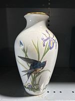 Front view of a white porcelain bird vase with a swallow and floral painting on body, gold rim visible on neck