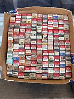 Top-down view of a box containing approximately 100 vintage vacuum tubes in original boxes. Labels visible include RCA, Raytheon, Sylvania, Philco, Tung-Sol, Admiral, Zenith, and others. Model numbers include various 6D and 6DT series tubes.
