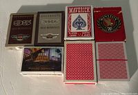 Seven decks of playing cards including branded and promotional themed decks, some unopened, some with box damage.