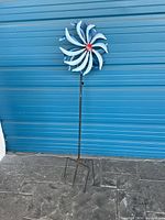 Full view of metal garden windmill showing spiral blue and white blades and red center on black pole with pronged base.