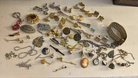 Overview of mixed preowned jewelry lot including cuff links, tie clips, pendants, and chains spread out on table.