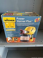 Box image showing the Wagner Power Stainer Plus, a heavy-duty stain sprayer for mid-sized projects. The box highlights features such as usage on fences, floors, decks, and siding with a flow rate of 6.6 liters per 24.98 minutes, suitable for exterior use.