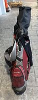 Full view of golf bag in red and black with Dunlop branding, standing on paved floor with clubs visible inside