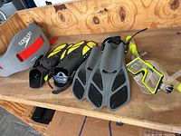 Photo showing Speedo branded gray life belt with red straps, a pair of yellow and black kid's fins, another pair of gray and black fins, two snorkeling masks with clear lenses and neon yellow frame, and two snorkels with neon yellow and black mouthpieces.