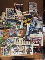 Wide view of assortment of baseball cards, football cards, magazines, trading cards, and other sports memorabilia spread on table.