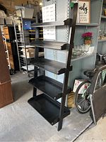 Black staggered leaning shelf with five shelves, photographed from a side angle showing the slight lean and varying shelf depths