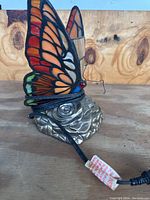 Photo of butterfly lamp side view showing stained glass wings with orange and red hues, black leading, and metal base with foliage design.