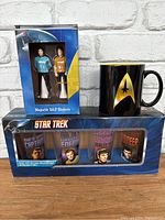 Full lot showing Star Trek salt and pepper shakers in box, black coffee mug with gold emblem, and a boxed set of four Star Trek glasses.