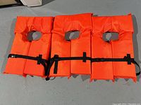 Photo of three new lifejackets laid side by side showing front with adjustable black buckle straps and neck openings.