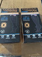 Two boxed pairs of Copper Fit Energy Compression Socks side by side on a cardboard surface.