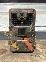 Front view of the trail camera showing the camo pattern, lens, infrared LED array, motion sensor, and latch