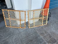 Photo of two beige metal pet sliding gates with diamond mesh design shown side by side on pavement next to a white wall.