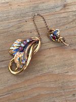 Vintage gold tone brooch set with enamel and pink gemstones, one clasp missing, shown on wooden surface.