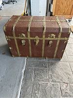 Front view of vintage trunk showing front buckle, lock, and brass straps.