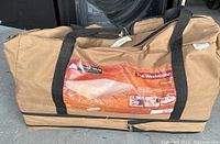 Brown carrying bag with black handles and zipper, showing product label for The Weekender Queen Size Cot and Inflatable Mattress.