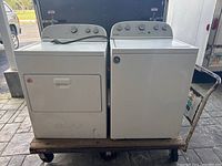 Photo of side-by-side Whirlpool washer and dryer on a wheeled dolly, showing exterior condition and setup.