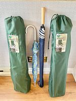 Two green Ozark Trail foldable camping chairs in carrying bags and two umbrellas: one smaller patterned umbrella with curved handle and one classic Sothebys golf umbrella with wooden handle.