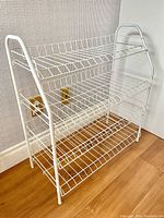 Front angled view of white metal 4 tier shoe rack placed near wall