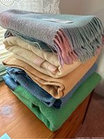 Stack of six wool blankets in a variety of colors on wooden surface