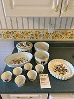Photo showing all items in the lot on kitchen counter: oval Evesham oven-to-table dish, Botanical Garden lidded casserole dish, fluted round quiche dish and six ramekins with fruit designs.