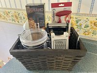 Photo showing basket with multiple kitchen gadgets including Paderno pineapple corer box, clear canister, Cuisipro apple corer packaging, and other utensils.