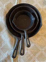 Set of three cast iron skillets stacked, showing size comparison and general condition