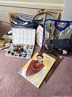 Collection of various cross stitch and crochet supplies including thread bags, thread organizer box, books, embroidery hoops, and thimbles.