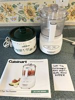 Photo showing the Cuisinart Mini Prep Plus food processor, Rival Little Dipper electric stoneware server, and Cuisinart instruction booklet on a countertop with floral wallpaper background.