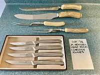 Top view of both steak knives set in box with serrated stainless steel blades and carving cutlery set with antler handles.