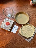 Set of items on wood floor including two stone-wear baking moulds, a mini digital kitchen scale in box, and a clear glass measuring cup.
