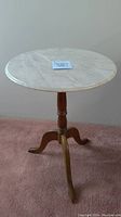 Full view of the side table showing round white marble top and wooden tripod base on carpeted floor.