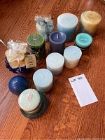 Twelve assorted pillar candles in shades of blue and green with three blue glass candle holders arranged on a wooden surface, some with labels and scent information visible.