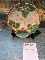 Front view of ceramic decorative plate with floral and leaf motifs and small inset turquoise dish section, displayed on black stand.