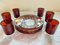 Set of 6 ruby red stemware glasses and 4 clear decorative plates arranged on a white surface.