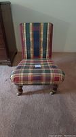 Front view of low plaid upholstered chair with wooden legs on casters.