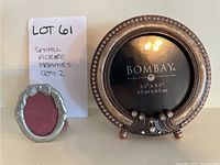 Two small oval pewter Seagull photo frames with bow design and maroon insert, and one round Bombay metal photo frame with decorative beading, standing upright on table.