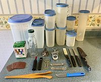 Full lot overview with Tupperware containers, glass jar, knives, tools, and kitchen utensils arranged on countertop.