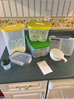 Various Tupperware containers of different sizes and colors with lids and accessories on kitchen counter.