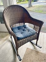Front angled view of the medium brown wicker rattan rocking chair with blue cushion, placed indoors near a door.