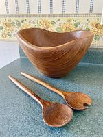 Photo of the wooden wave salad bowl and two wooden salad spoons on a countertop, showing the bowl's shape and wood grain surfaces.