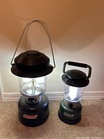 Photo showing both Coleman lanterns positioned side by side, highlighting their size difference and overall condition.