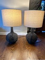 Pair of table lamps on wooden floor, beige linen-like shades and rope-wrapped geometric bases