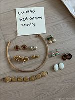 Photo of 1980s costume jewelry lot including gold-tone choker, multiple pairs of stud and clip-on earrings and a textured gold bracelet.