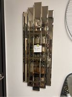 Full front view of the vertical Art Deco style mirror mounted on wall, showing stepped multiple beveled mirrored panels and reflection of room behind.