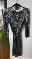 Front view of black vintage flapper dress decorated with silver beadwork and sequins hanging on a wall hook.