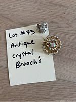 Two vintage crystal rhinestone brooches on wooden background next to a handwritten note describing them as antique crystal brooches
